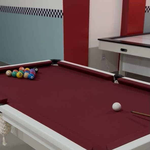 Mesa de sinuca com as bolas montadas no triângulo, o hockey de mesa ao fundo e a faixa xadrez na parede