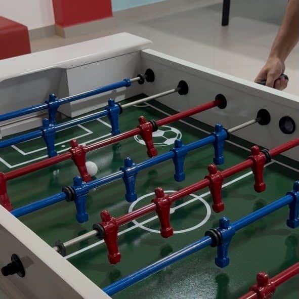 Mão no punho do totó no meio da partida, com a bola em jogo sobre o campo verde